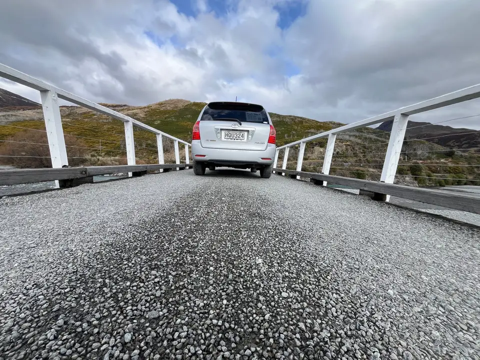 From behind on a one-lane bridge, mountains in the distance