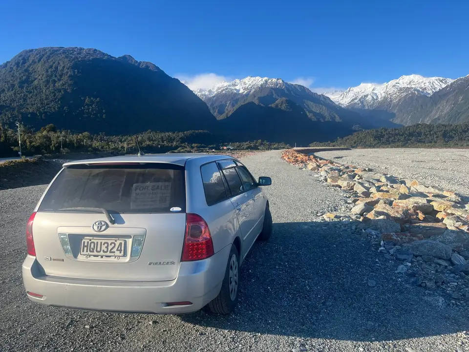 Parked on gravel above the river with snowy peaks beyond