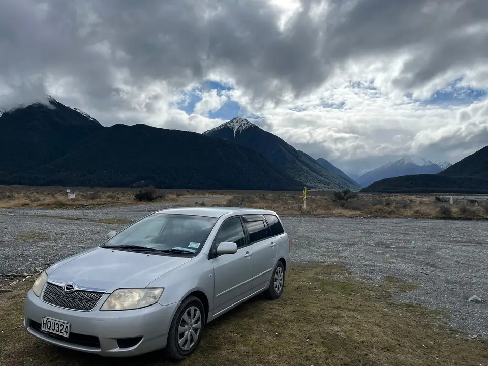 Parked on river flats under a bank of cloud and mountains