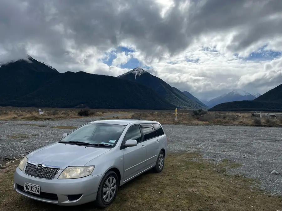 Parked on river flats under a bank of cloud and mountains
